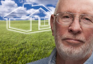 Melancholy senior man with green grass field and ghosted house behind him