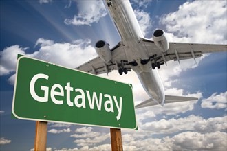 Getaway green road sign and airplane above with dramatic blue sky and clouds