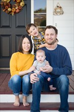 Young mixed-race chinese and caucasian family portrait on their front porch