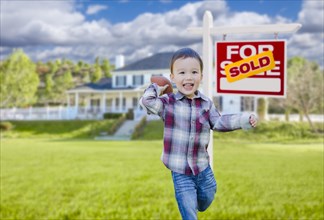 Cute mixed-race boy playing ball in front yard near sold real estate sign