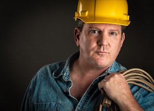 Serious contractor in hard hat holding extension cord with dramatic lighting