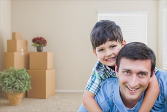 Happy father and son in room with packed moving boxes and potted plants