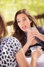 Expressive young adult woman having drinks and talking with her friend outdoors