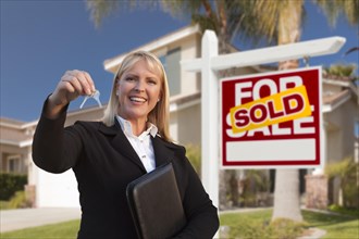 Female real estate agent handing over the house keys in front of a beautiful new home and real estate sign