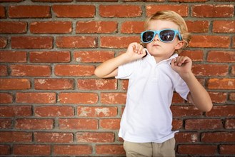 Cute young caucasian boy wearing sunglasses against brick wall
