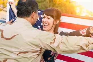 Excited woman with american flag runs to male military soldier returning home