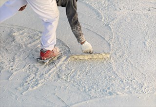 Worker wearing spiked shoes smoothing wet pool plaster with trowel