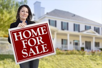 Smiling hispanic female holding sold for sale sign in front of beautiful house