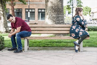 Unhappy mixed-race couple sitting facing away from each other on park bench