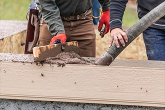 Construction workers pouring and leveling wet cement into wood framing