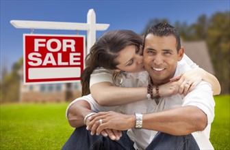 Young happy hispanic young couple in front of their new home and for sale real estate sign