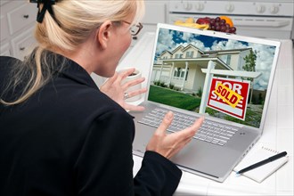 Excited woman in kitchen using laptop to sell or buy a home. screen can be easily used for your own message or picture. picture on screen is my copyright as well