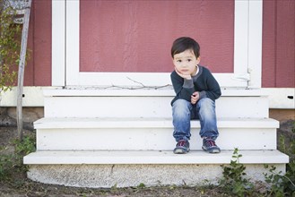 Cute mixed-race boy sitting relaxed on the steps on a barn