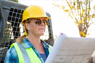 Female worker holding technical blueprints near small bulldozer at construction site