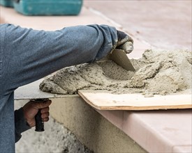 Tile worker mixing wet cement on board at pool construction site