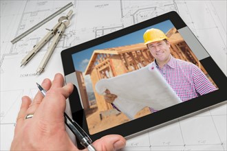 Hand of architect on computer tablet showing contractor and home framing photo over house plans