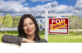 Pretty hispanic woman leaning on white in front of beautiful house and sold for sale real estate sign