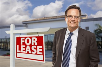 Handsome businessman in front of vacant office building and for lease real estate sign