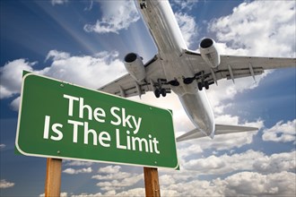 The sky is the limit green road sign and airplane above with dramatic blue sky and clouds