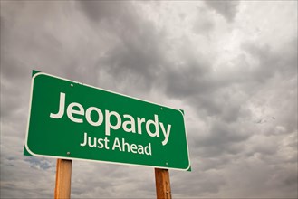 Jeopardy just ahead green road sign with dramatic storm clouds and sky