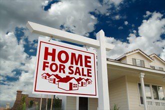 Red home for sale real estate sign and house against a blue sky