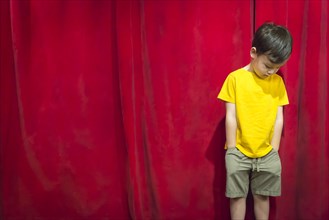 Sad pouting mixed-race boy standing in front of red curtain