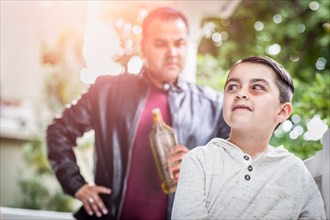 Afraid and bruised mixed-race boy in front of angry man holding bottle of alcohol