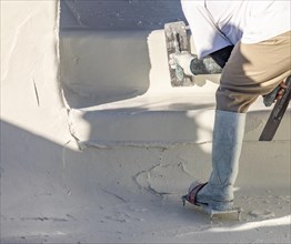 Worker wearing spiked shoes smoothing wet pool plaster with trowel