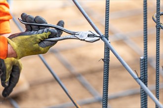 Worker securing steel rebar framing with wire plier cutter tool at construction site