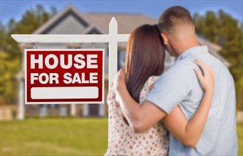 For sale real estate sign and affectionate military couple looking at nice new house
