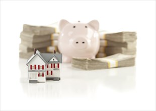 Small house and piggy bank with stacks of hundred dollar bills isolated on a white background