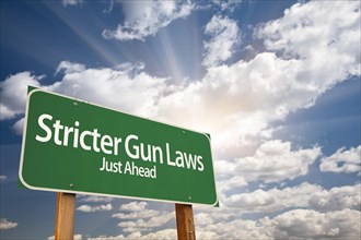 Stricter gun laws green road sign with dramatic clouds and sky
