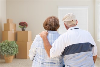 Senior couple facing empty room with packed moving boxes and potted plants