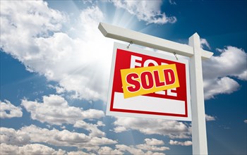 Sold for sale real estate sign over clouds and blue sky with sun rays