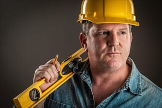 Serious contractor in hard hat holding level and pencil with dramatic lighting