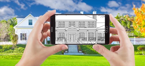 Hands holding smart phone displaying drawing of custom home photo behind