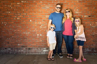 Young caucasian family wearing sunglasses against brick wall