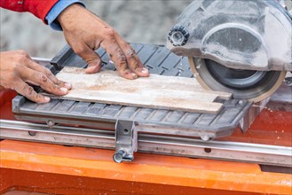 Worker using wet tile saw to cut wall tile at construction site