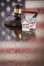 Small house and gavel on wooden table with american flag reflection