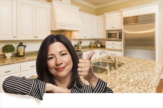 Hispanic woman with thumbs up in custom kitchen interior leaning on white
