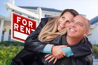 Happy couple hugging in front of for rent real estate sign and house