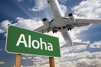 Aloha green road sign and airplane above with dramatic blue sky and clouds