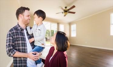 Young mixed-race caucasian and chinese family inside empty room with wood floors