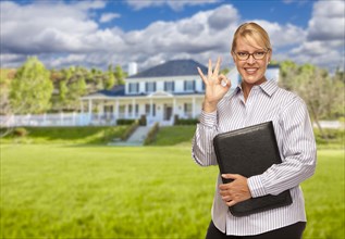 Attractive businesswoman with okay hand sign in front of nice residential home