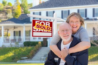 Senior adult couple in front of sold home for sale real estate sign and beautiful house
