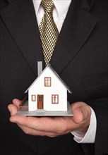 Businessman with coat and tie holding house