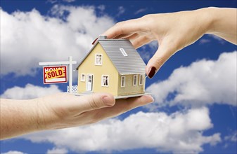 Reaching for A home with sold real estate sign on a bright blue cloudy sky background