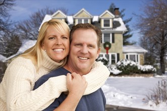 Happy couple in front of beautiful house with snow on the ground