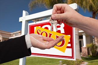 Agent handing over the key to a new home with real estate sign and house in the background