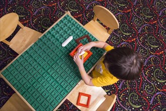 Overhead of mixed-race boy sitting at a work table playing with building blocks toys